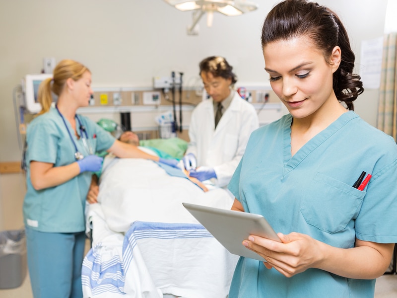 Beautiful nurse using digital tablet while doctor and colleague operating male patient in hospital